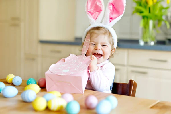 Cute little toddler girl wearing Easter bunny ears playing with colored pastel eggs. Happy baby child unpacking gifts. Adorable kid in pink clothes enjoying holiday — Stock Photo, Image