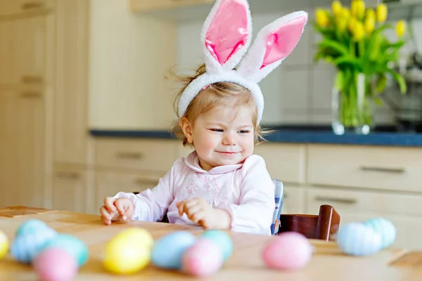 Cute little toddler girl wearing Easter bunny ears playing with colored pastel eggs. Happy baby child unpacking gifts. Adorable kid in pink clothes enjoying holiday — Stock Photo, Image