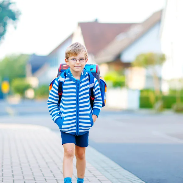 Fröhlicher kleiner Junge mit Brille und Rucksack oder Schulranzen auf dem Weg zur Schule oder in den Kindergarten. Kind an warmen, sonnigen Tagen im Freien, zurück zur Schule, Bildungskonzept. — Stockfoto