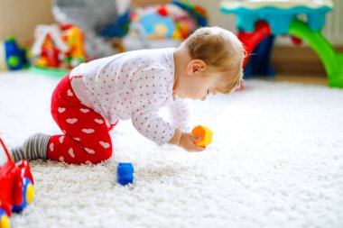 Küçük şirin bebek kız tarama öğrenme. Sağlıklı çocuk çocuk odası renkli oyuncaklar ile kaynıyor. Bebek bacakları arkadan görünüm. Ana sayfa keşfetmek ve farklı becerileri öğrenme şirin bebek