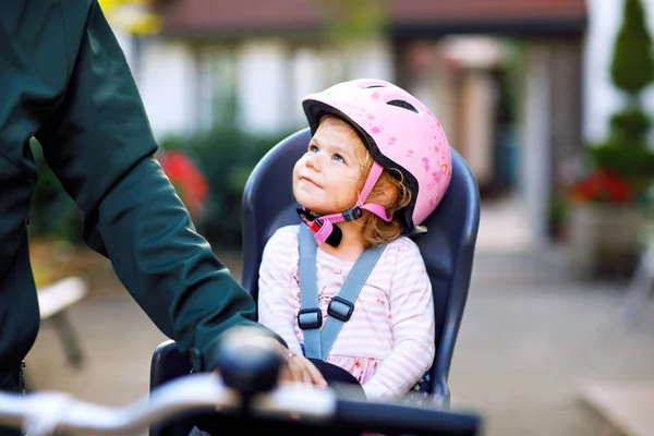 自転車の座席に座って頭の上にセキュリティヘルメットを持つ小さな幼児の少女の肖像画と自転車で彼女の父や母親。安全で子供の保護の概念。家族や週末のアクティビティ旅行. — ストック写真