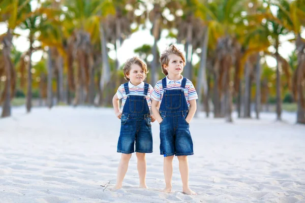 Dos niños pequeños divirtiéndose en la playa tropical, felices mejores amigos jugando, concepto de amistad. Hermanos hermanos, gemelos en familia miran con palmas en el fondo. Vacaciones familiares en el océano . —  Fotos de Stock