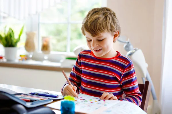 Gelukkig lachend jongetje dat thuis huiswerk maakt op de ochtend voor de school begint. Klein kind aan het sporten, binnen. Basisschool en onderwijs: Jongenstekening geometrische figuren — Stockfoto