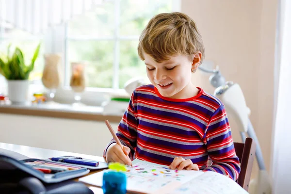 Buon bambino sorridente a casa a fare i compiti la mattina prima dell'inizio della scuola. Un bambino che fa esercizio, in casa. Scuola elementare e istruzione: Ragazzo disegno figure geometriche — Foto Stock