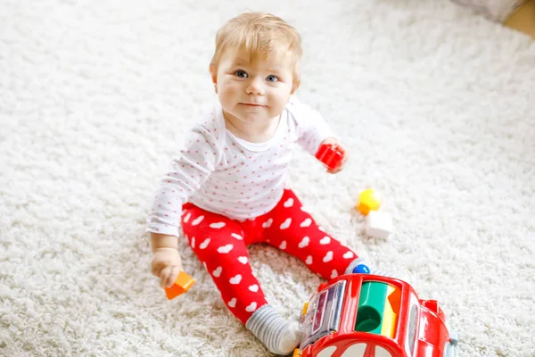 Schattig leuk mooie babymeisje spelen met houten onderwijsspeelgoed thuis of kwekerij. Gezonde happy peuter met kleurrijke rode auto binnenshuis. kinderen leren kleuren en vormen — Stockfoto