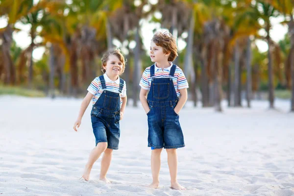 Due bambini piccoli ragazzi che si divertono sulla spiaggia tropicale, felici migliori amici che giocano, concetto di amicizia. Fratelli fratelli, i gemelli in occhiata di famiglia con palme su sfondo. Vacanze in famiglia sull'oceano . — Foto Stock