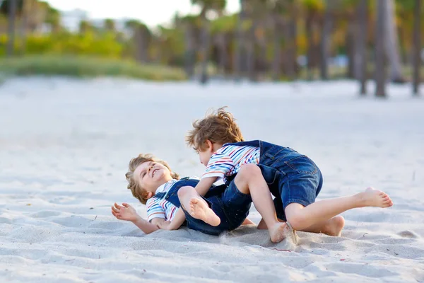 Dos niños pequeños divirtiéndose en la playa tropical, felices mejores amigos jugando, concepto de amistad. Hermanos hermanos, gemelos peleando, corriendo y saltando en mirada familiar con palmeras en el fondo. — Foto de Stock