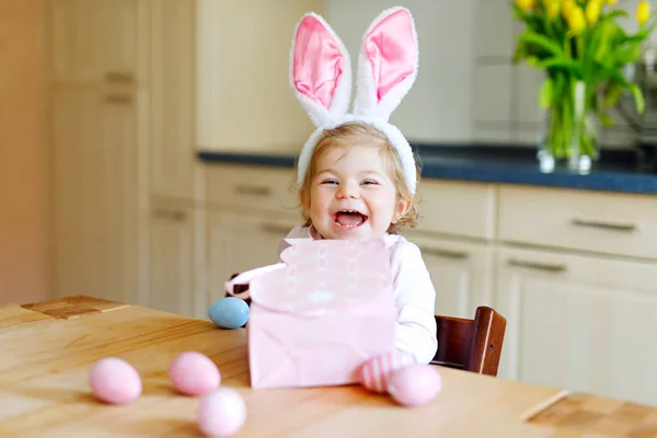 Roztomilá malá batole dívka, která nosí Velikonoční zajíček uši hrát s barevnými pastelovými vajec. Happy baby dítě rozbalování dárků. Rozkošné dítě v růžové oblečení těší dovolená — Stock fotografie