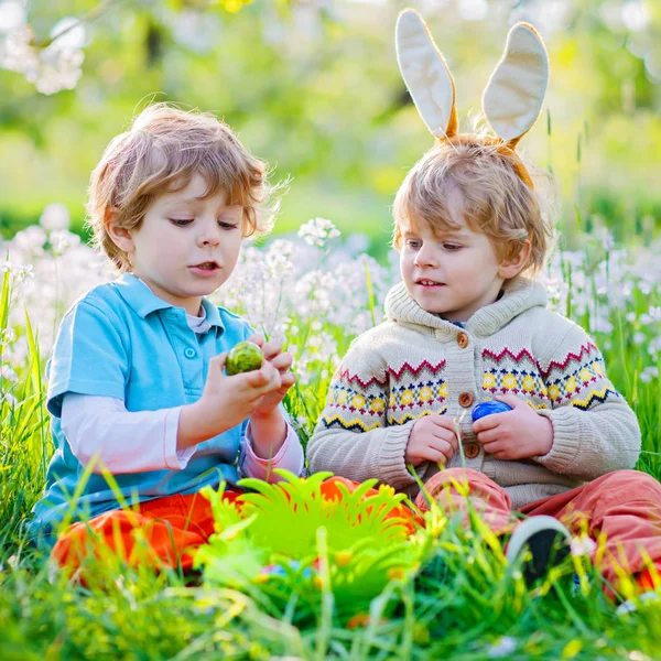 Cute adorable little kid boy making an egg hunt on Easter. Happy child searching and finding colorful eggs in domestic garden. Boy in spring clothes on cold day. Old christian and catholoc tradition. — Stock Photo, Image