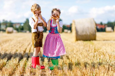 Buğday tarlasında geleneksel Bavyera kostümlü iki çocuk. Alman çocukları Ekim Festivali sırasında ekmek ve simit yiyorlar. Almanya 'da yaz aylarında erkek ve kız saman balyalarında oynuyorlar..