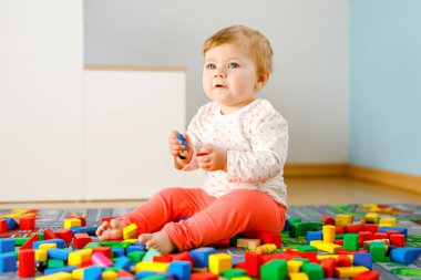 Eğitici oyuncaklarla oynayan sevimli bir kız bebek. Mutlu sağlıklı bir çocuk, evdeki renkli tahta bloklarla eğleniyor. Bebek öğrenme renkleri ve biçimleri