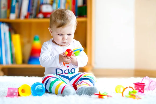 Bebek odasında eğitici oyuncaklarla oynayan sevimli bir kız. Mutlu sağlıklı çocuk evde renkli farklı oyuncaklarla eğleniyor. Bebek gelişimi ve ilk adımlar, çalmayı ve yakalamayı öğrenmek.. — Stok fotoğraf