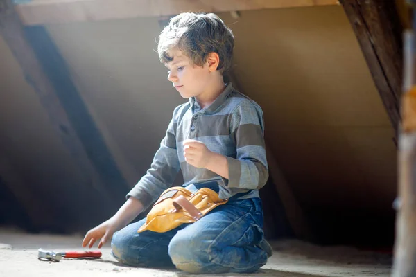 Ragazzino che aiuta con gli attrezzi giocattolo sul cantiere. Bambino divertente di 6 anni che si diverte a costruire una nuova casa di famiglia. Ragazzo con chiodi e martello che aiuta il padre a ristrutturare la vecchia casa. — Foto Stock