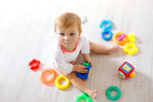 Adorable niña jugando con juguetes educativos en la guardería. Feliz niño sano que se divierte con diferentes juguetes de colores en casa. Niño tratando de construir la pirámide de plástico y el uso de bloques con letras —  Fotos de Stock