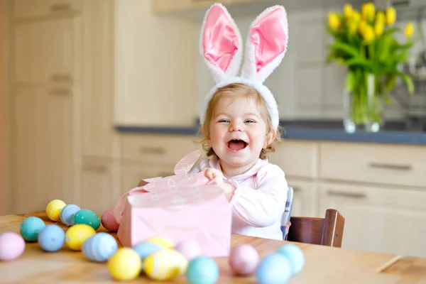 Cute little toddler girl wearing Easter bunny ears playing with colored pastel eggs. Happy baby child unpacking gifts. Adorable healthy smiling kid in pink clothes enjoying family holiday — Stock Photo, Image