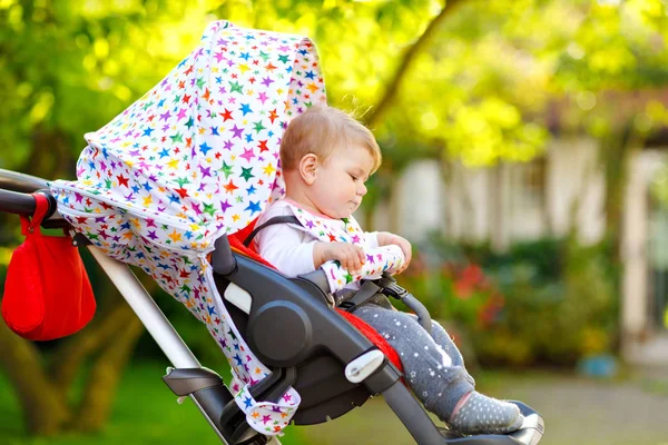 Cute zdrowe małe piękne dziecko dziewczynka siedzi w wózku lub wózek i czeka na mamę. Szczęśliwe uśmiechnięte dziecko z niebieskimi oczami. Z zielonym tłem drzewa. Mała córeczka idzie na spacer z rodziną — Zdjęcie stockowe