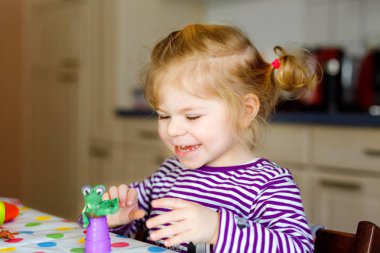 Renkli killi, sevimli, küçük bir kız. Sağlıklı bebek oyun oynuyor ve oyun hamurundan oyuncaklar yapıyor. Küçük çocuk kil kalıp ve öğrenim