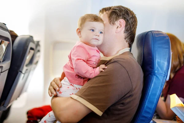 Middle-aged father and his crying baby daughter during flight on airplane going on vacations. Dad holding and playing with baby girl on arm. Air travel with baby, child and family concept — Stock Photo, Image