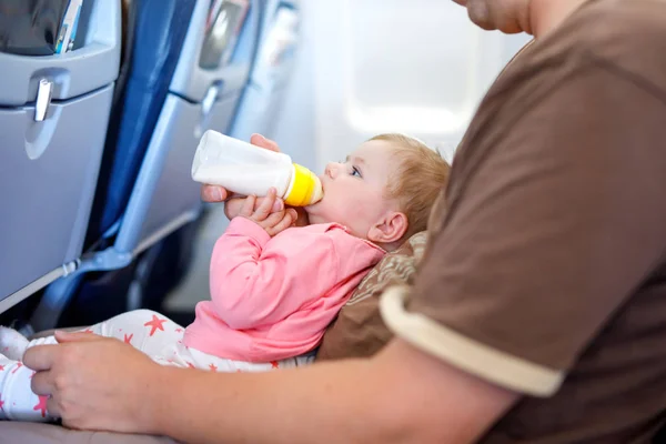 Ojciec trzymający córeczkę podczas lotu na samolocie wybierasz się na wakacje. Dziewczynka picia mleka z butelki. Air travel z koncepcji dla niemowląt, dzieci i rodziny. Zmęczony człowiek podróże z dziećmi. — Zdjęcie stockowe