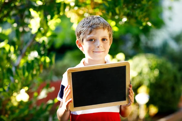 Happy little kid boy with chalk desk in hands. Healthy adorable child outdoors Empty desk for copyspace holding by beautiful schoolkid — Stock Photo, Image