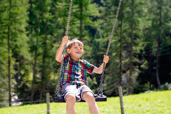 Chico divertido que se divierte con el oscilación de la cadena en el patio al aire libre mientras está mojado salpicado con agua. niño balanceándose en el día de verano. Ocio activo con niños. Feliz niño llorando con gotas de lluvia en la cara. — Foto de Stock