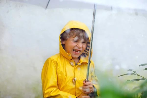 Beautiful little kid boy on way to school walking during sleet, heavy rain and snow with an umbrella on cold day. Happy and joyful child in colorful yellow coat fashion casual clothes — Stock Photo, Image