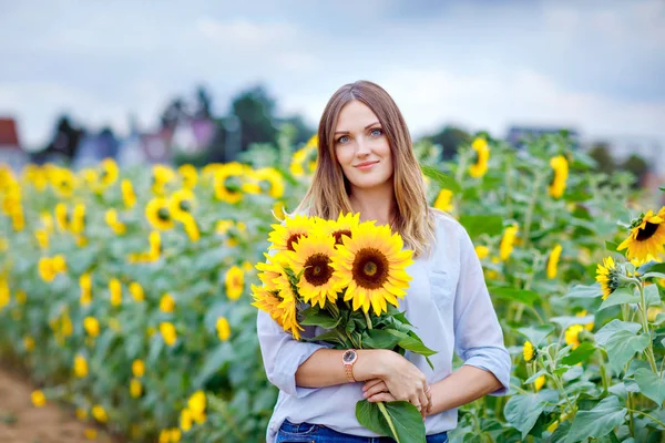 Mooie jonge vrouw op zonnebloemenveld met boeket bloemen. gelukkig meisje op zomer zonsondergang dag. — Stockfoto