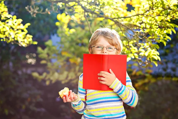 Счастливый маленький мальчик дошкольного возраста с очками, книгами, яблоком и рюкзаком в свой первый день в школу или ясли. Забавный здоровый ребенок на свежем воздухе в теплый солнечный день, концепция "Вернуться в школу". Смеющийся мальчик. — стоковое фото