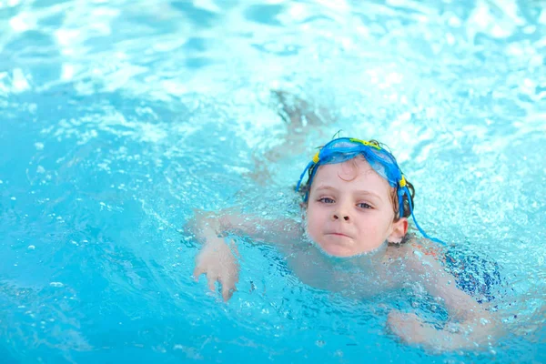Маленький мальчик из детского сада делает соревнования по плаванию. Ребенок в очках для плавания достигает края бассейна. Ребенок веселится в бассейне. Активный счастливый ребенок выигрывает. спорт, активный отдых . — стоковое фото