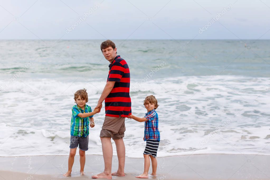 Two happy little kids boys and father standing on the beach of ocean and looking on horizon on stormy day. Family, dad and cute sons making vacations, dreaming and enjoying summer