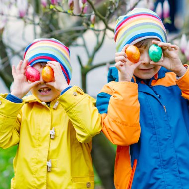 İki küçük çocuklar ve arkadaşlar bahar bahçe, açık havada AVI geleneksel Paskalya yortusu yumurta yapma çocuk. Kardeşler renkli yumurta bulma ile eğleniyor. Soğuk günde. Eski Hıristiyan ve Katolik gelenek.