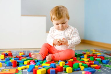 Eğitici oyuncaklarla oynayan sevimli bir kız bebek. Mutlu sağlıklı bir çocuk, evdeki renkli tahta bloklarla eğleniyor. Bebek öğrenme renkleri ve biçimleri