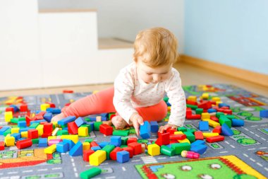 Eğitici oyuncaklarla oynayan sevimli bir kız bebek. Mutlu sağlıklı bir çocuk, evdeki renkli tahta bloklarla eğleniyor. Bebek öğrenme renkleri ve biçimleri