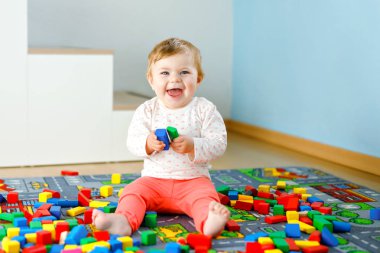 Eğitici oyuncaklarla oynayan sevimli bir kız bebek. Mutlu sağlıklı bir çocuk, evdeki renkli tahta bloklarla eğleniyor. Bebek öğrenme renkleri ve biçimleri