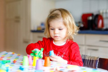 Renkli killi, sevimli, küçük bir kız. Sağlıklı bebek oyun oynuyor ve oyun hamurundan oyuncaklar yapıyor. Küçük çocuk kil kalıp ve öğrenim
