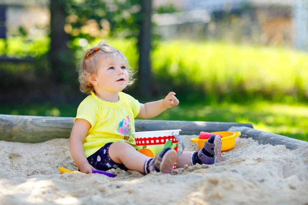 Söt liten flicka leker i sand på utomhus lekplats. Vackra baby att ha kul på solig varm sommar solig dag. Glad frisk barn med sandleksaker och i färgglada mode kläder. — Stockfoto