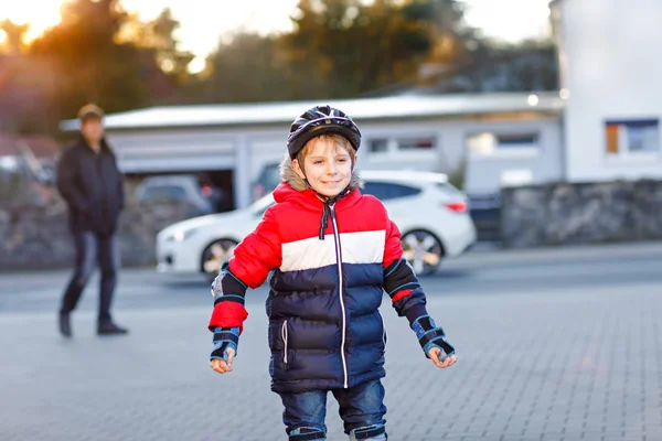 Niño de escuela y padre patinando con patinadores en la ciudad. Feliz niño sano en la protección de la ropa de seguridad y papá. Colegial activo haciendo deporte y aprendiendo a patinar en patinador en línea . —  Fotos de Stock