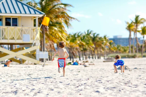 Dos niños pequeños divirtiéndose en la playa tropical, felices mejores amigos jugando con arena, concepto de amistad. Hermanos caldos en pantalones de natación cazando gaviotas. Key Biscayne, Miami, Florida . —  Fotos de Stock