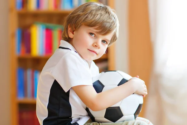 Little blond preschool kid boy with ball watching soccer football cup game on tv. Funny happy crying child fan having fun and cheering winning football team. Champions and world cup concept — Stock Photo, Image
