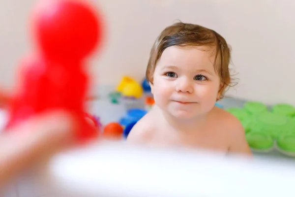 Милая очаровательная малышка, принимающая пенную ванну в ванной. Тоддлер играет с резиновыми игрушками. Красивый ребенок веселится с красочными игрушками жевательной резинки и пеной пузырьков — стоковое фото