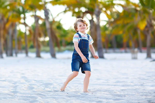Miami sahilinde eğlenen sevimli, aktif bir çocuk, Key Biscayne. Mutlu şirin çocuk rahatlıyor, kumla oynuyor ve palmiyelerin ve okyanusun yanında güneşli bir günün tadını çıkarıyor. — Stok fotoğraf