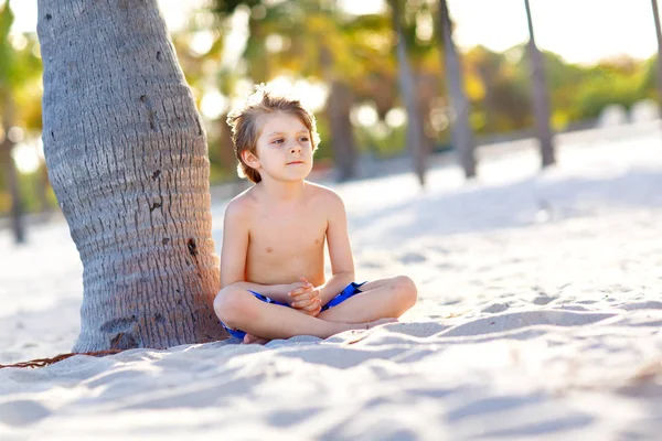 Blond little kid boy having fun on Miami beach, Key Biscayne. Happy healthy cute child playing with sand and running near ocean. Palms, security house and white sand. With sunny warm bright light — Stock Photo, Image