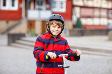 Okula giderken ya da dönerken scooter 'a binen şirin bir okul çocuğu. Yedi yıllık öğrenci yağmur birikintisinin içinden geçiyor. renkli elbiseli ve kasklı komik mutlu çocuk..