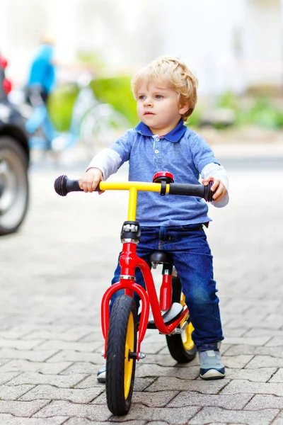Aktív szőke fiú színes ruhában vezetés egyensúly és a tanulók kerékpár vagy kerékpár a hazai kertben. Kisgyermek álmodik, és jól érzi magát a meleg nyári napon. szabadtéri mozgás játék gyerekeknek — Stock Fotó