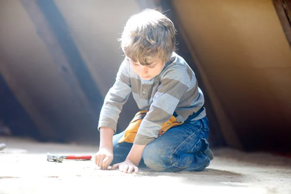 Menino ajudando com ferramentas de brinquedo no canteiro de obras. Criança engraçada de 6 anos se divertindo na construção de uma nova casa de família. Criança com unhas e martelo ajudando o pai a renovar a casa velha. — Fotografia de Stock