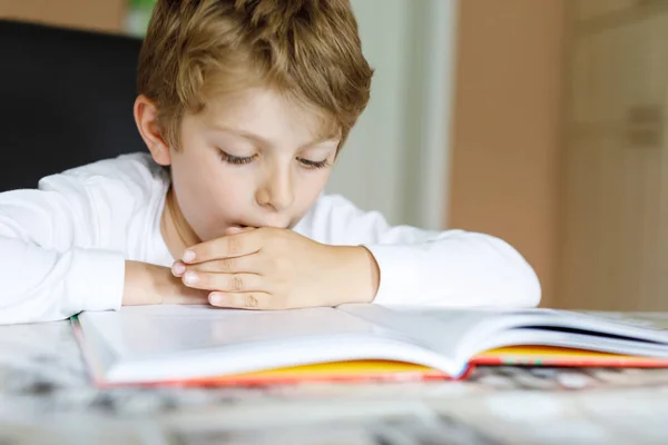 En blond skolpojke som läser en bok hemma. Barn intresserade av att läsa tidningen för barn. Fritid för barn, bygga färdigheter och utbildning koncept — Stockfoto