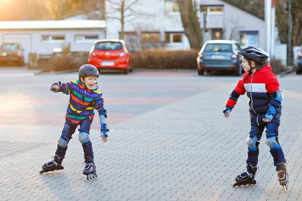 Twee kleine jongens schaatsen met rollers in de stad. Gelukkige kinderen, broers en zussen en beste vrienden in beschermende veiligheidskleding. Actieve schooljongens die sport maken en leren schaatsen op inline skater. — Stockfoto