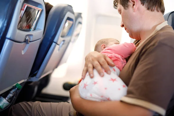 Young tired father and his baby daughter sleeping during flight on airplane going on vacations. Dad holding baby girl on arm. Air travel with baby, child and family concept — Stock Photo, Image