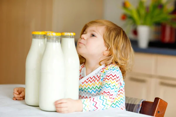 Schattig peutermeisje dat koemelk drinkt als ontbijt. Schattige kleine dochter met veel flessen. Gezond kind dat melk als gezondheidscalciumbron heeft. Kind thuis of in de kinderkamer in de ochtend. — Stockfoto