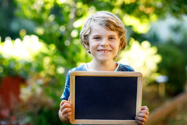 手にチョークの机を持つ幸せな子供の男の子。健康かわいい子供屋外コピースペースのために保持する美しい学童 — ストック写真